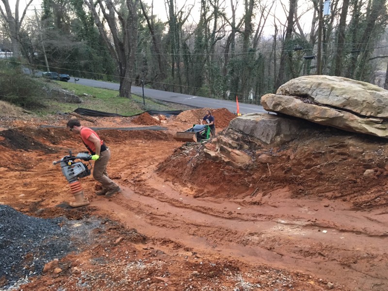 Reid using a jumping jack to pack down the loose earth and John using a standing skid steer to creating an even 15% grade